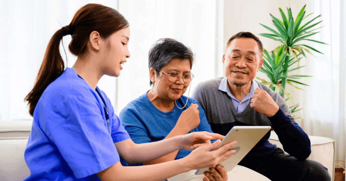 Healthcare staff explaining eye screening information on a tablet to an older Asian couple.