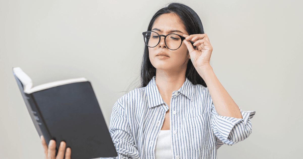 Woman adjusting glasses while is difficult to reading a book because of hyperopia
